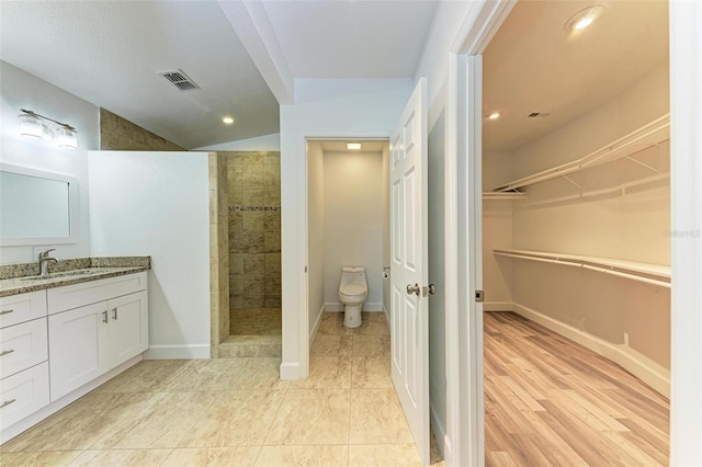 bathroom featuring tiled shower, toilet, vanity, and wood-type flooring