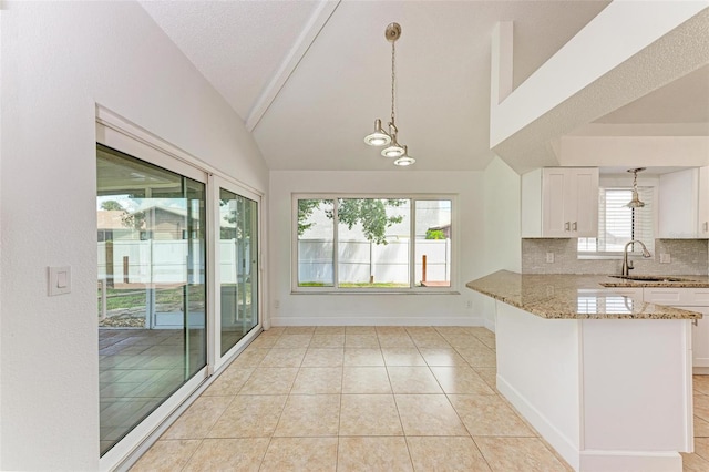 kitchen with lofted ceiling, white cabinets, kitchen peninsula, sink, and light stone countertops