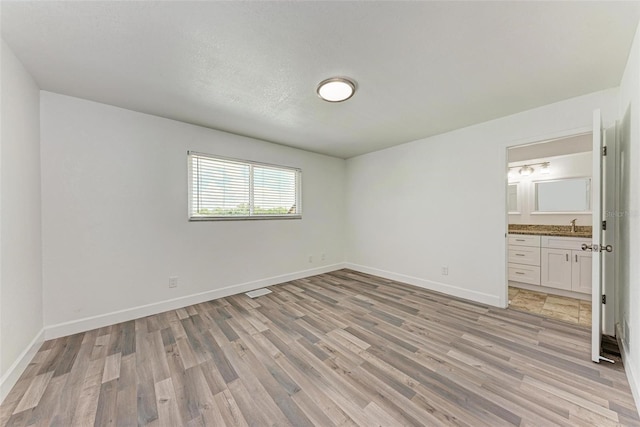 unfurnished bedroom featuring light hardwood / wood-style floors, connected bathroom, and sink