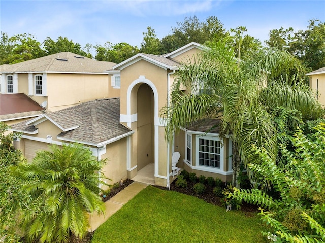 view of front facade featuring a shingled roof, a front yard, and stucco siding