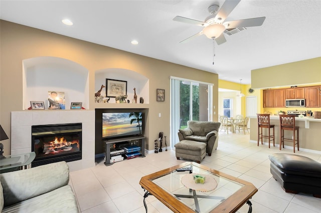 tiled living room with ceiling fan and a tile fireplace