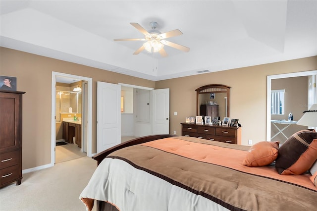 carpeted bedroom featuring ceiling fan, ensuite bathroom, and a tray ceiling