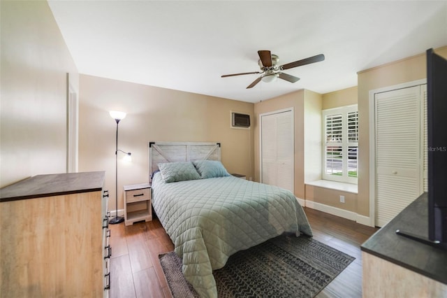 bedroom featuring two closets, a ceiling fan, a wall mounted AC, wood finished floors, and baseboards