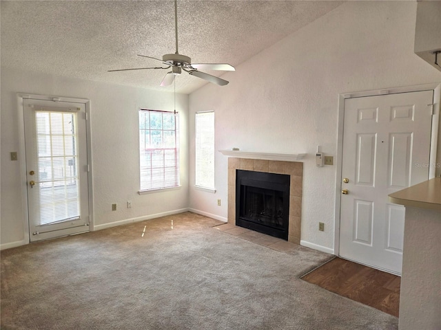 unfurnished living room featuring a textured ceiling, vaulted ceiling, a tiled fireplace, light carpet, and ceiling fan