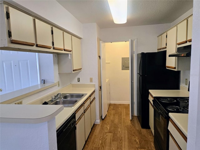 kitchen with a textured ceiling, black appliances, sink, cream cabinetry, and hardwood / wood-style flooring