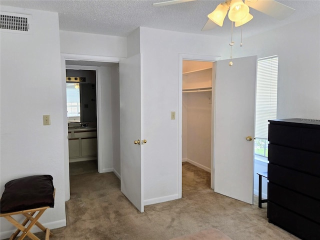 bedroom with multiple windows, ceiling fan, a walk in closet, and light carpet