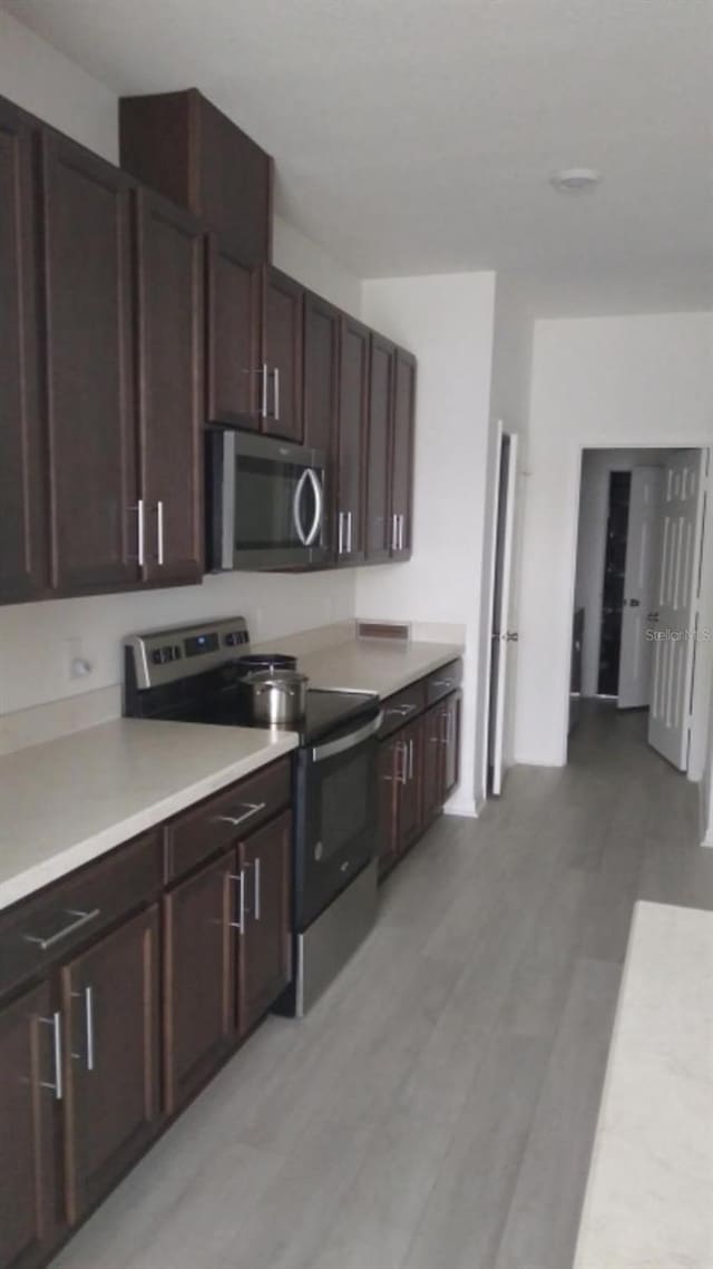 kitchen featuring appliances with stainless steel finishes, light wood-type flooring, and dark brown cabinetry