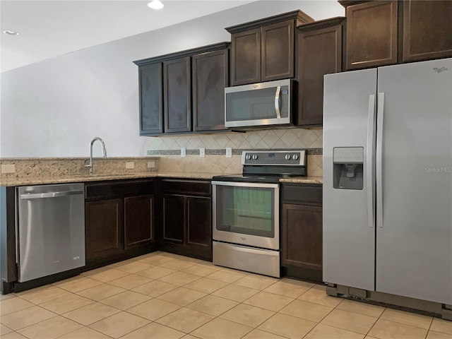 kitchen with a sink, tasteful backsplash, appliances with stainless steel finishes, light stone countertops, and dark brown cabinets