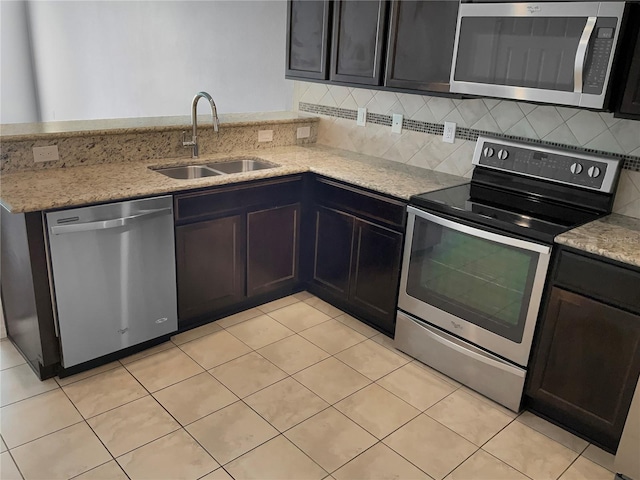 kitchen with appliances with stainless steel finishes, light tile patterned floors, light stone countertops, and sink