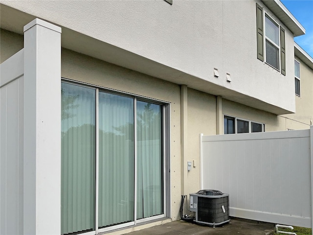 view of side of property featuring stucco siding, central AC unit, and fence