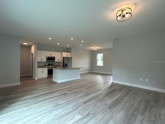 kitchen with stainless steel appliances, open floor plan, white cabinetry, and wood finished floors