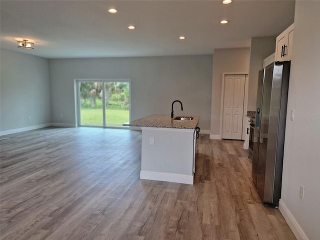 kitchen with light wood-style flooring, a sink, light stone countertops, stainless steel fridge, and a center island with sink