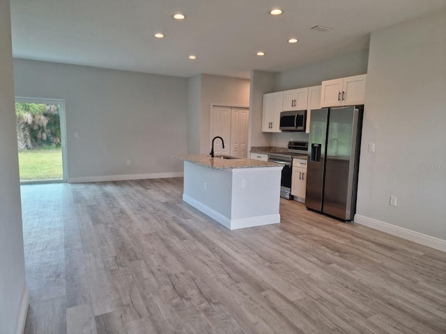 kitchen with light hardwood / wood-style flooring, light stone counters, an island with sink, appliances with stainless steel finishes, and white cabinets