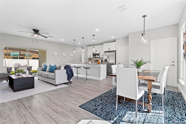 dining space featuring light hardwood / wood-style flooring, sink, and ceiling fan with notable chandelier