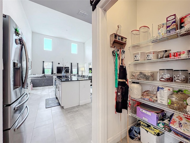 kitchen with a towering ceiling, light tile patterned floors, stainless steel fridge with ice dispenser, and white cabinets