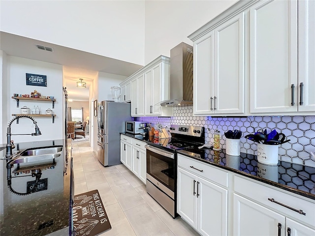 kitchen with wall chimney range hood, dark stone countertops, stainless steel appliances, and sink