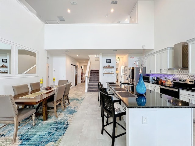 kitchen featuring stainless steel appliances, a kitchen breakfast bar, decorative backsplash, a towering ceiling, and wall chimney exhaust hood