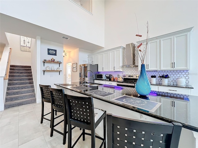 kitchen featuring dark stone countertops, stainless steel appliances, decorative backsplash, light tile patterned flooring, and wall chimney range hood