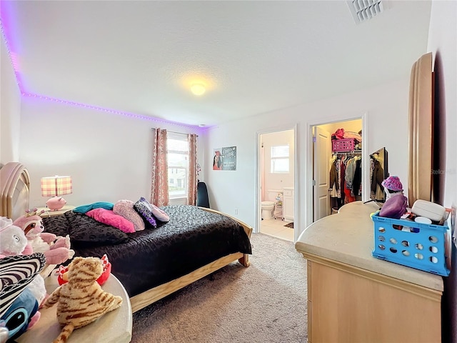 bedroom featuring ensuite bathroom, light colored carpet, a walk in closet, a closet, and a textured ceiling