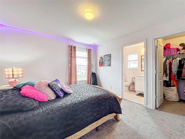 bedroom featuring ensuite bath, light colored carpet, a closet, a spacious closet, and a textured ceiling