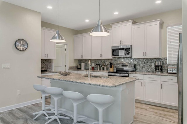 kitchen featuring white cabinetry, light stone counters, an island with sink, sink, and appliances with stainless steel finishes