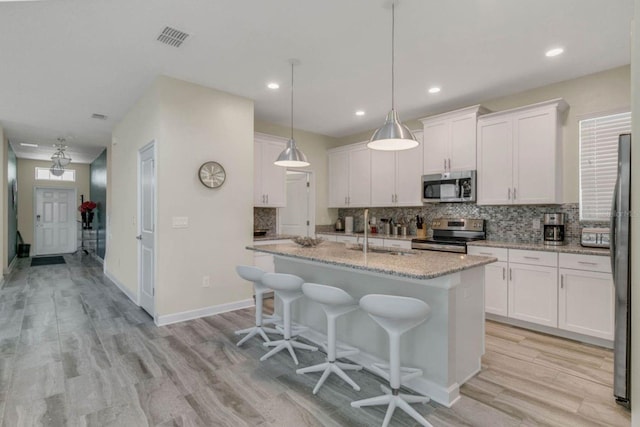 kitchen with a kitchen island with sink, white cabinetry, light stone counters, sink, and appliances with stainless steel finishes