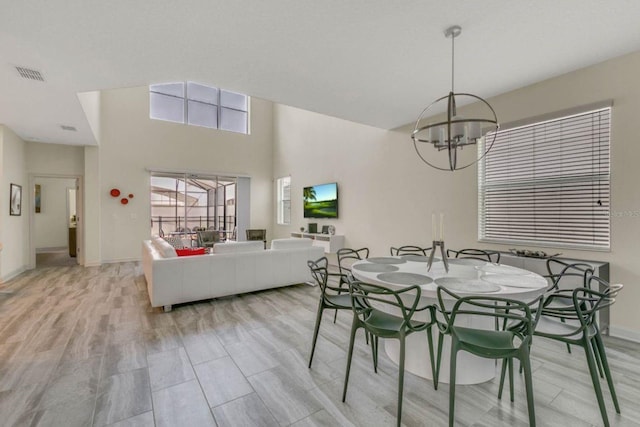 dining space featuring light hardwood / wood-style flooring, a chandelier, and a high ceiling