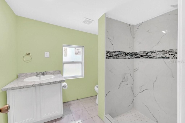 bathroom with a tile shower, vanity, and toilet