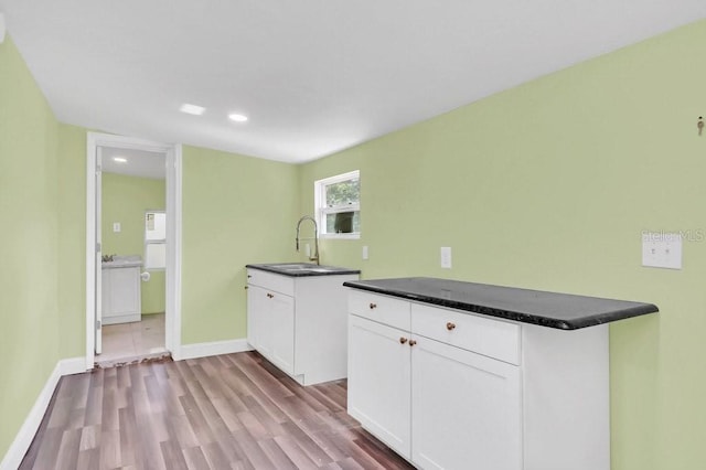 kitchen with kitchen peninsula, white cabinetry, sink, and light hardwood / wood-style flooring