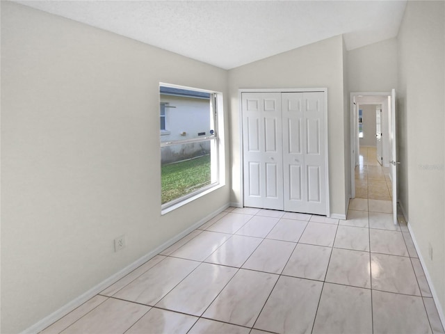 unfurnished bedroom featuring vaulted ceiling, a textured ceiling, light tile patterned flooring, and a closet