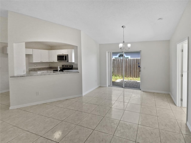 kitchen with a chandelier, light tile patterned floors, stainless steel appliances, vaulted ceiling, and white cabinets