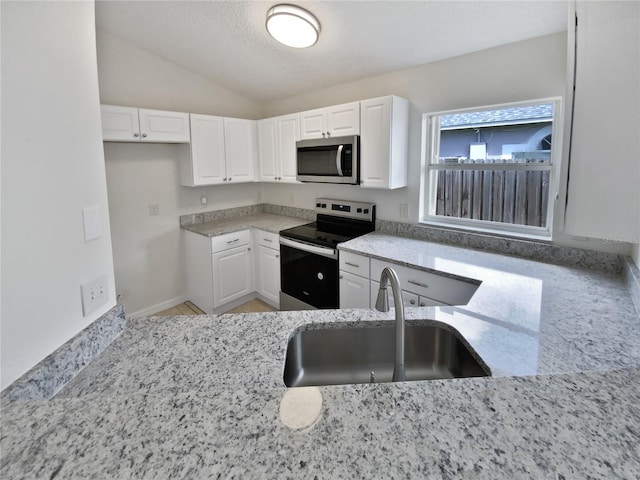 kitchen with white cabinetry, stainless steel appliances, light stone counters, sink, and vaulted ceiling