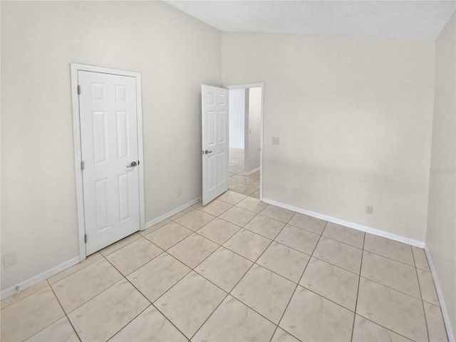 unfurnished room with vaulted ceiling and light tile patterned floors