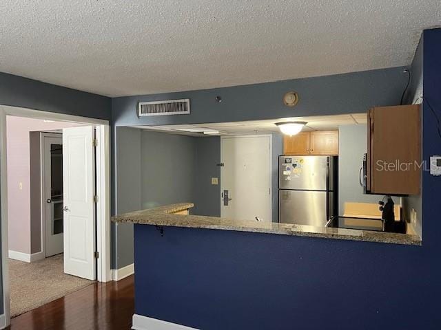 kitchen with appliances with stainless steel finishes, a textured ceiling, kitchen peninsula, and dark wood-type flooring