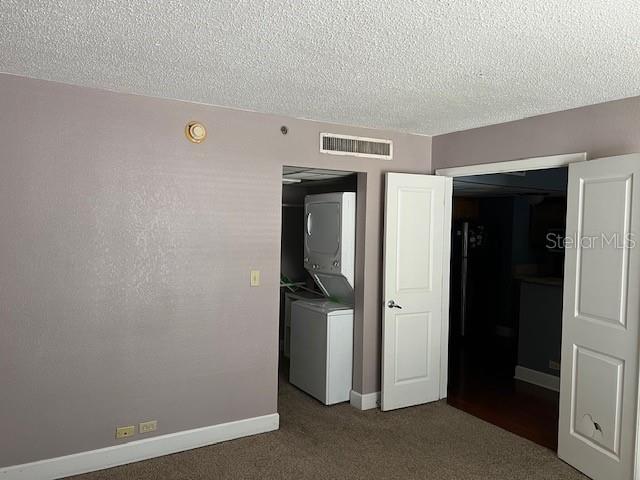 empty room with carpet floors, a textured ceiling, and stacked washer / dryer