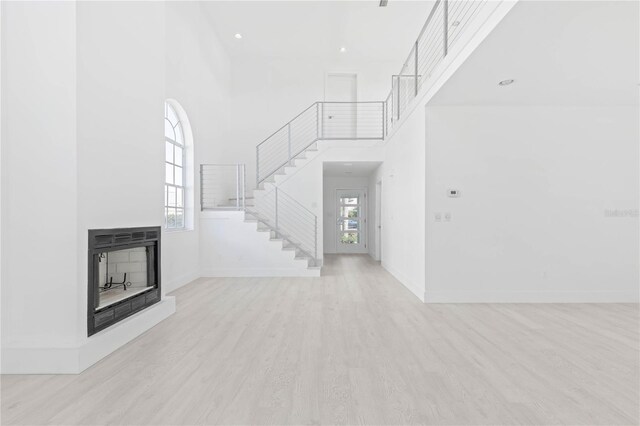 unfurnished living room featuring a towering ceiling, a multi sided fireplace, and light wood-type flooring