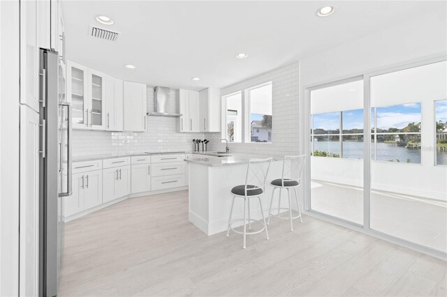 kitchen with a breakfast bar area, wall chimney exhaust hood, a water view, and white cabinetry