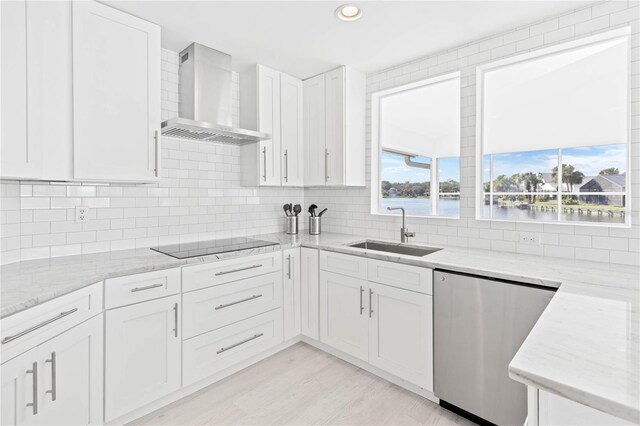 kitchen with white cabinets, sink, stainless steel dishwasher, wall chimney exhaust hood, and light hardwood / wood-style flooring