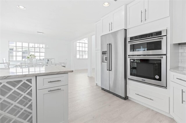 kitchen featuring appliances with stainless steel finishes, light hardwood / wood-style floors, tasteful backsplash, and white cabinetry