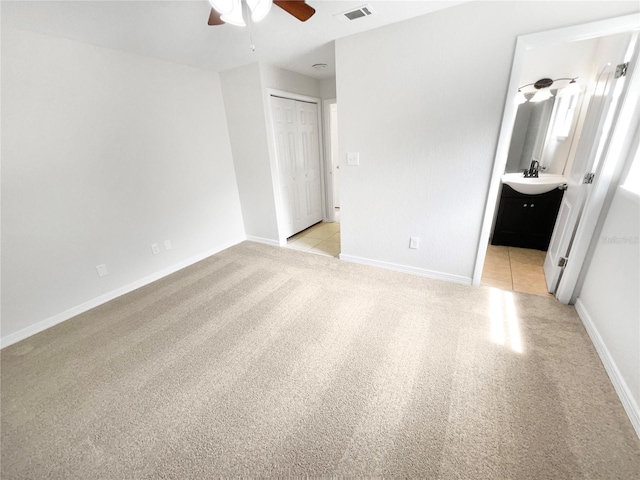 unfurnished bedroom with light carpet, sink, a closet, ceiling fan, and connected bathroom