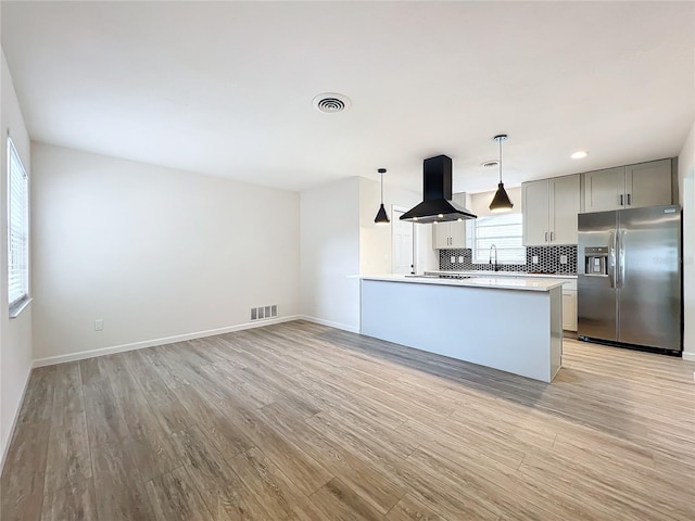 kitchen featuring light wood-type flooring, stainless steel fridge, decorative light fixtures, island range hood, and kitchen peninsula