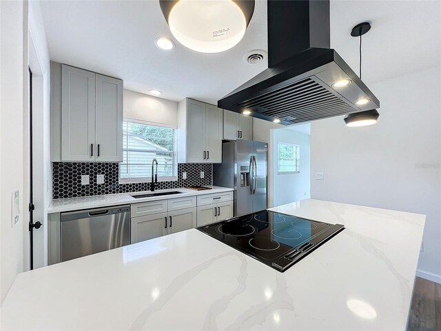 kitchen featuring decorative light fixtures, light stone countertops, appliances with stainless steel finishes, island range hood, and sink