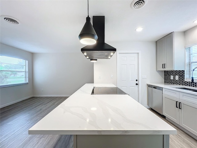 kitchen featuring island exhaust hood, light stone counters, stainless steel dishwasher, and light hardwood / wood-style floors