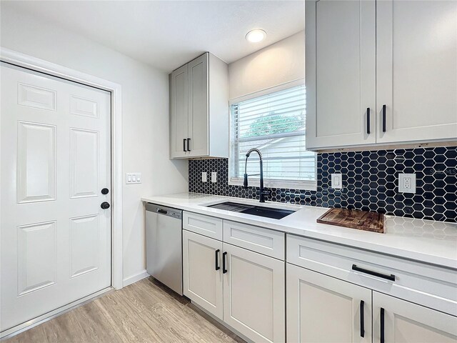 kitchen with tasteful backsplash, stainless steel dishwasher, sink, and light hardwood / wood-style floors