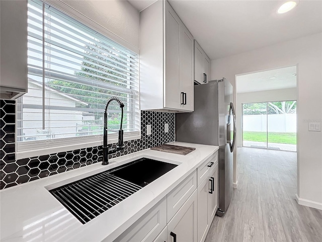 kitchen featuring white cabinets, stainless steel fridge, light hardwood / wood-style floors, and sink