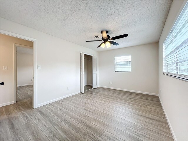 unfurnished bedroom with a textured ceiling, ceiling fan, a closet, and light wood-type flooring