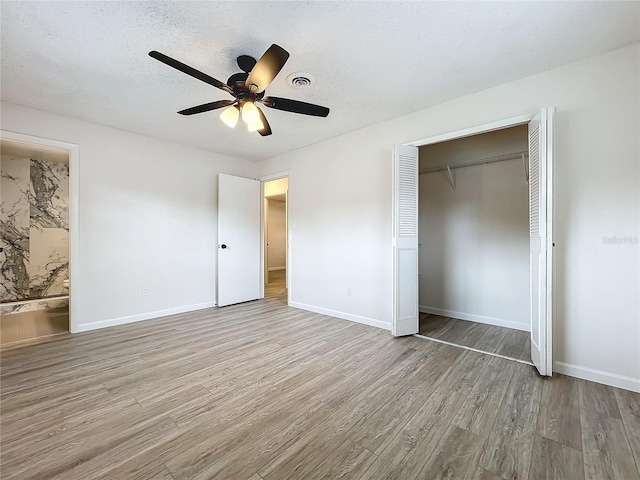 unfurnished bedroom featuring light wood-type flooring, a textured ceiling, ensuite bath, ceiling fan, and a closet