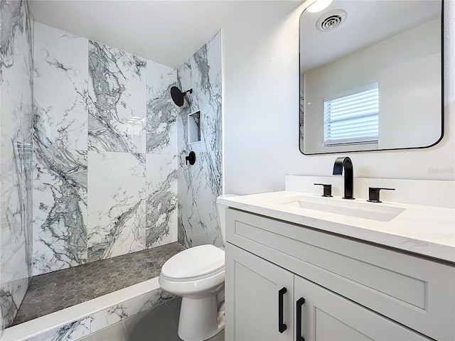 bathroom with tiled shower, toilet, and vanity