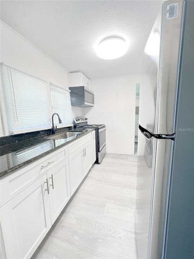 kitchen featuring sink, white cabinetry, appliances with stainless steel finishes, dark stone countertops, and light hardwood / wood-style floors