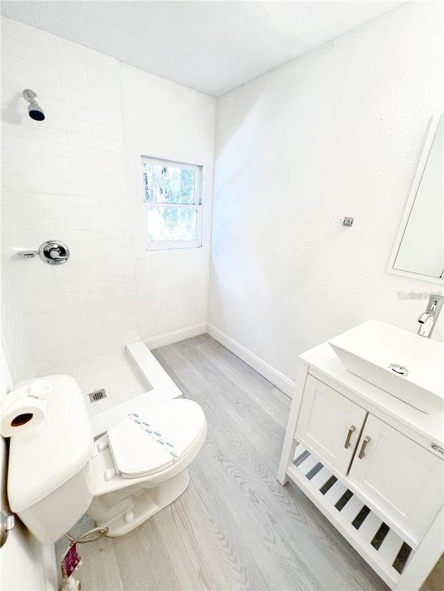 bathroom featuring a tile shower, hardwood / wood-style flooring, vanity, and toilet